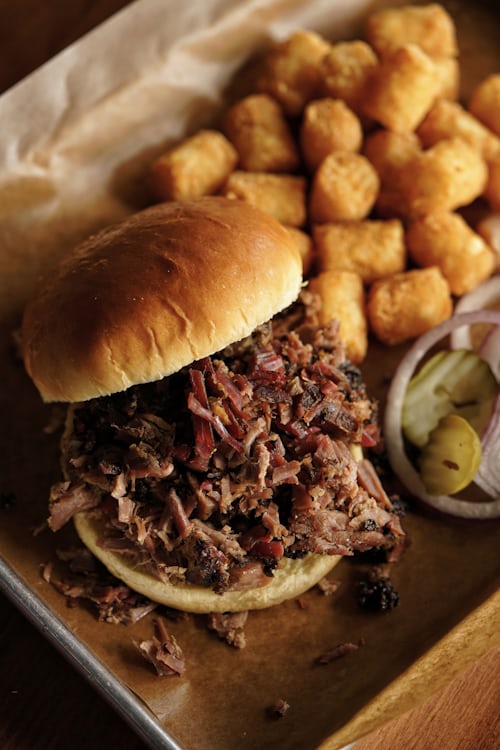 Pulled Pork Sandwich auf einem Tablett – saftiges gezupftes Schweinefleisch mit dunkler Bark auf einem Bun