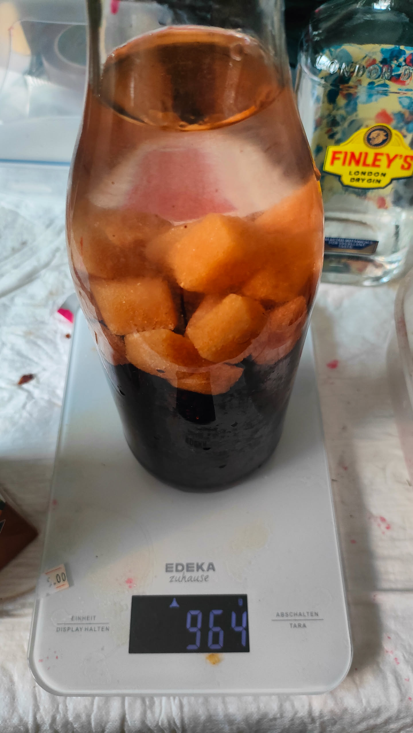 Glas mit Brombeeren, Zucker und aufgefülltem Gin auf der Waage, Anzeige 964 Gramm