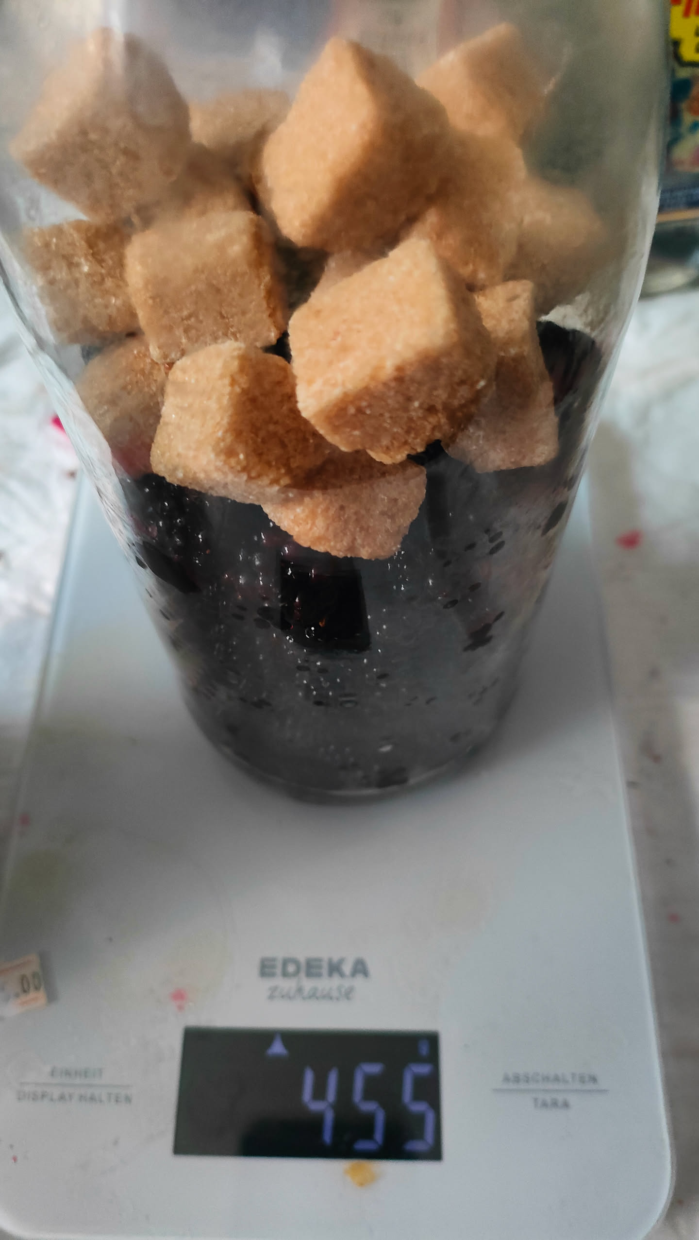 Braune Zuckerwürfel auf den Brombeeren im Glas, Waage zeigt 455 Gramm
