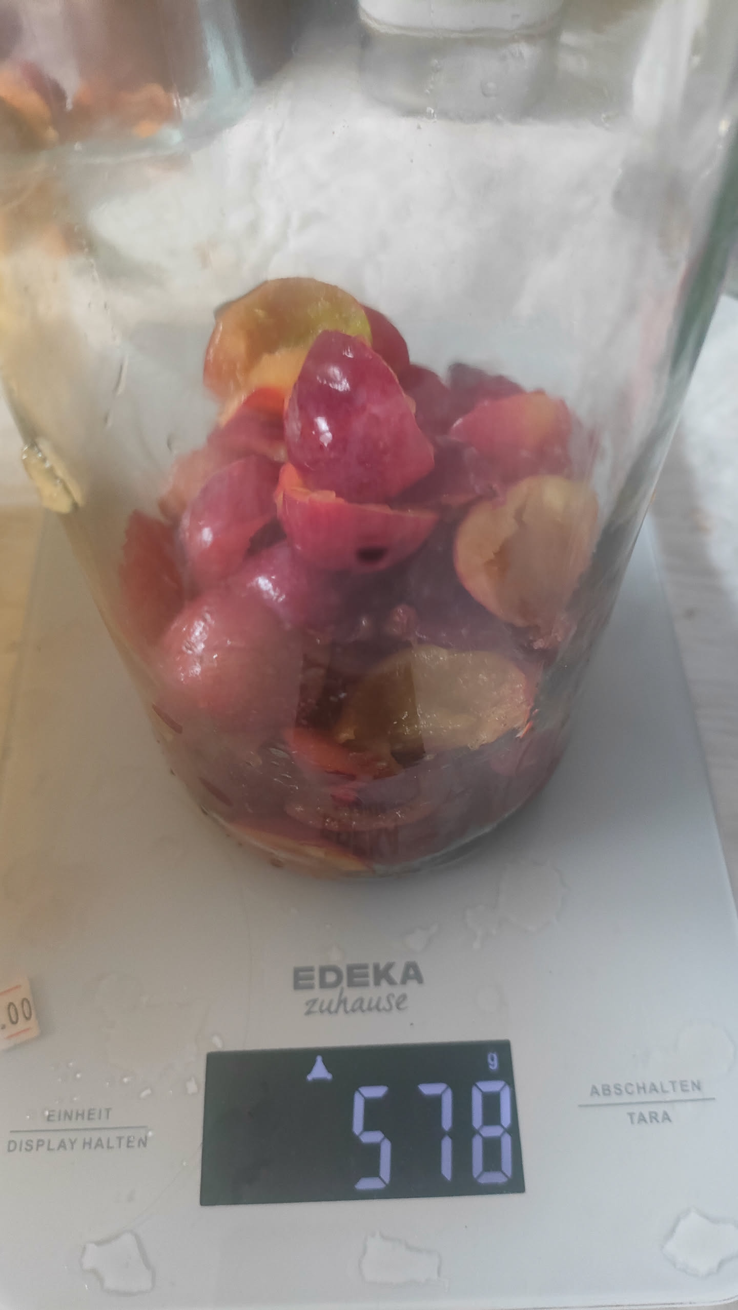 Halbierte, entkernte Kirschpflaumen in einem Glas auf einer Küchenwaage, Anzeige 578 Gramm