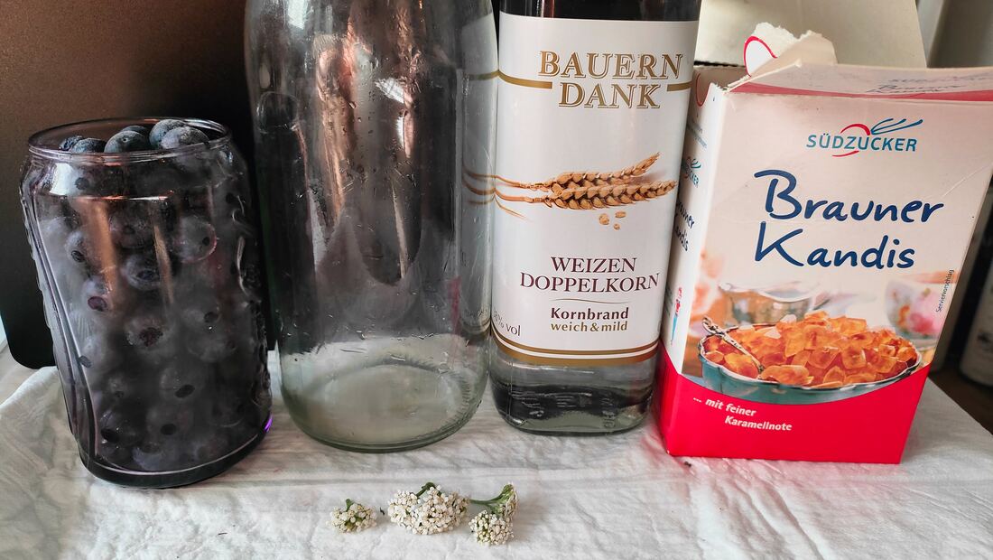 Zutaten für den zweiten Schlehenlikör-Ansatz: Schlehen im Glas, leere Flasche, Doppelkorn, brauner Kandis und drei weiße Schafgarbenblüten
