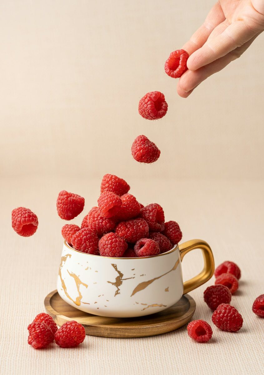Frische Himbeeren fallen in eine Tasse, Basis für Himbeerlikör