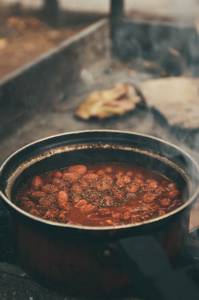 Chili con Carne mit Kidneybohnen brodelt in einem Topf über offenem Lagerfeuer