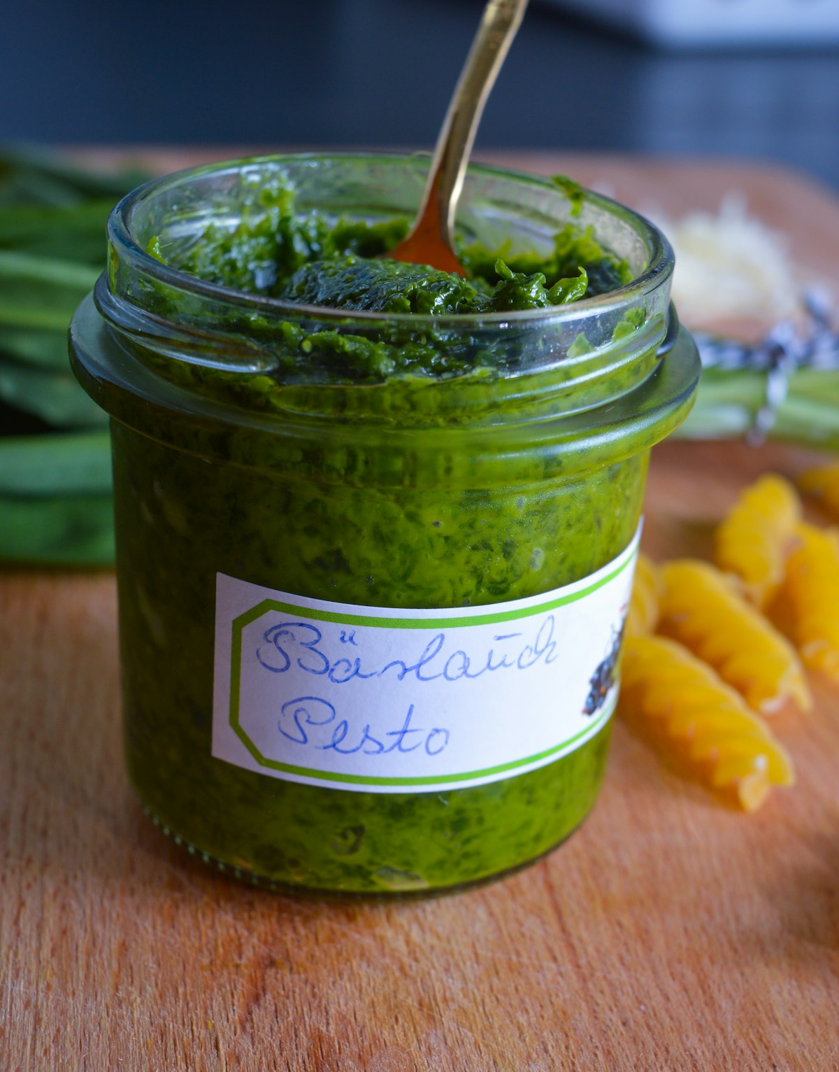 Bärlauch-Pesto im Glas, daneben frische Bärlauchblätter und Pinienkerne auf einem Holzbrett
