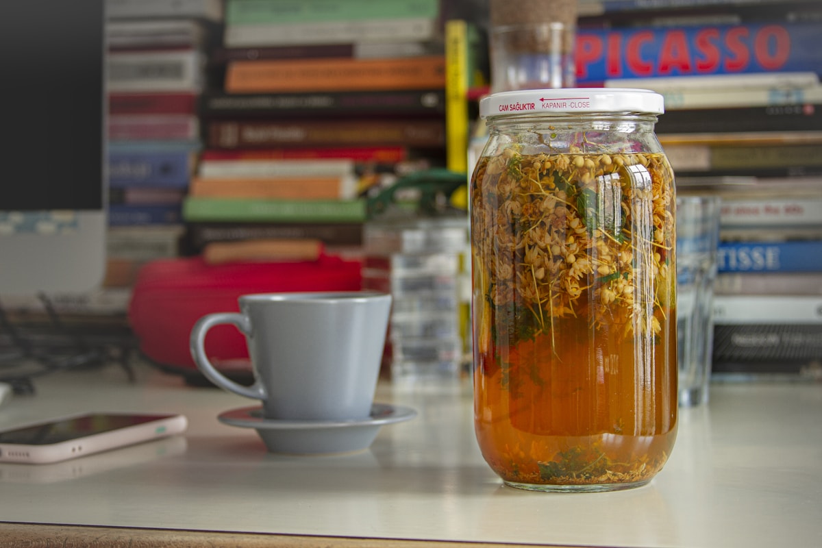 Kräutertee im Einmachglas mit Tasse daneben – Brennnesseln ziehen im heißen Wasser