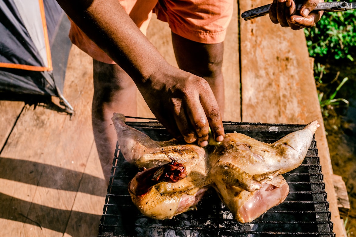 Geflügel auf einem Grillrost im Freien, jemand legt es auf, Zelt im Hintergrund