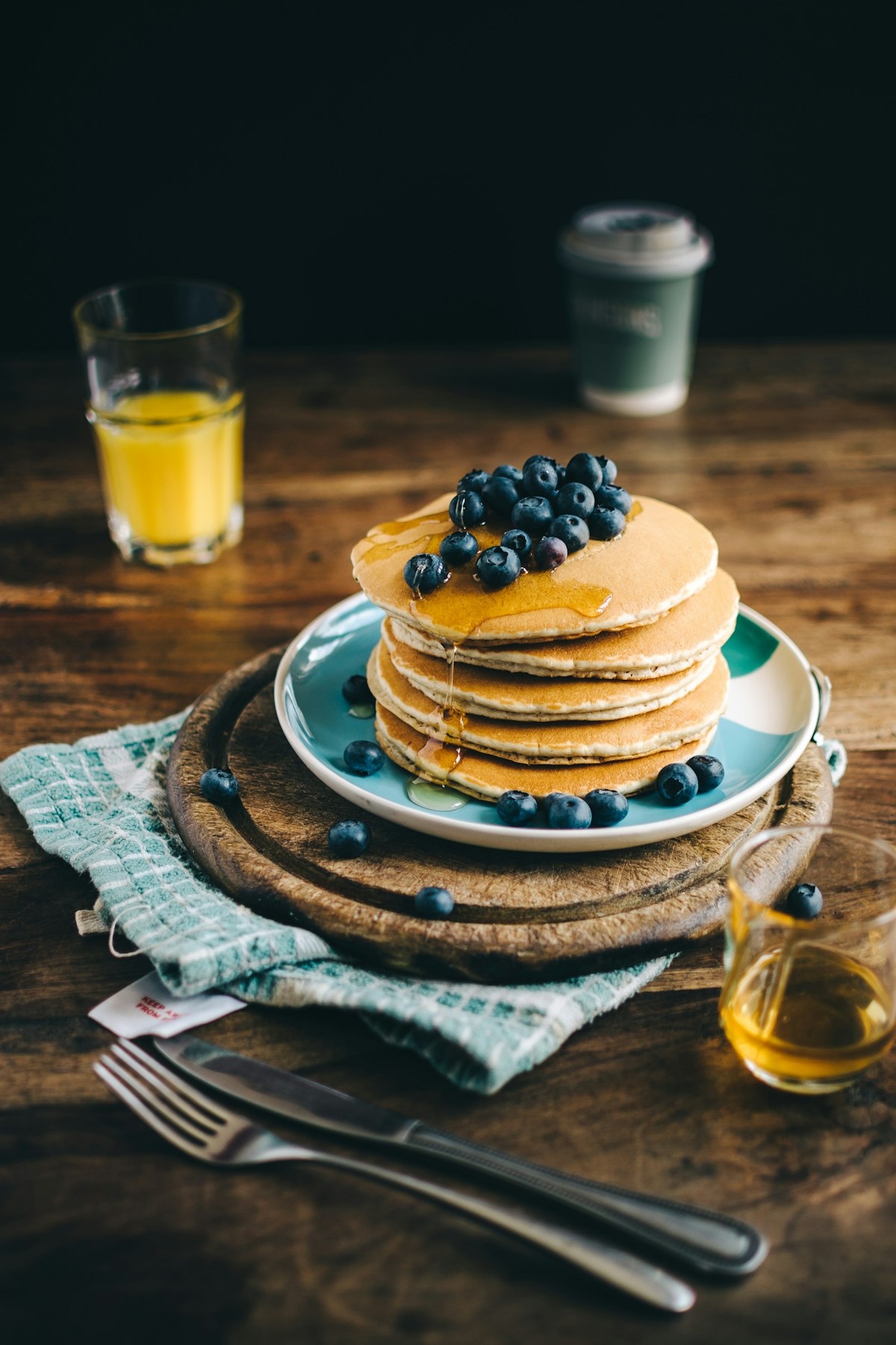Stapel goldbrauner Pfannkuchen mit Heidelbeeren und Ahornsirup auf rustikalem Holzbrett