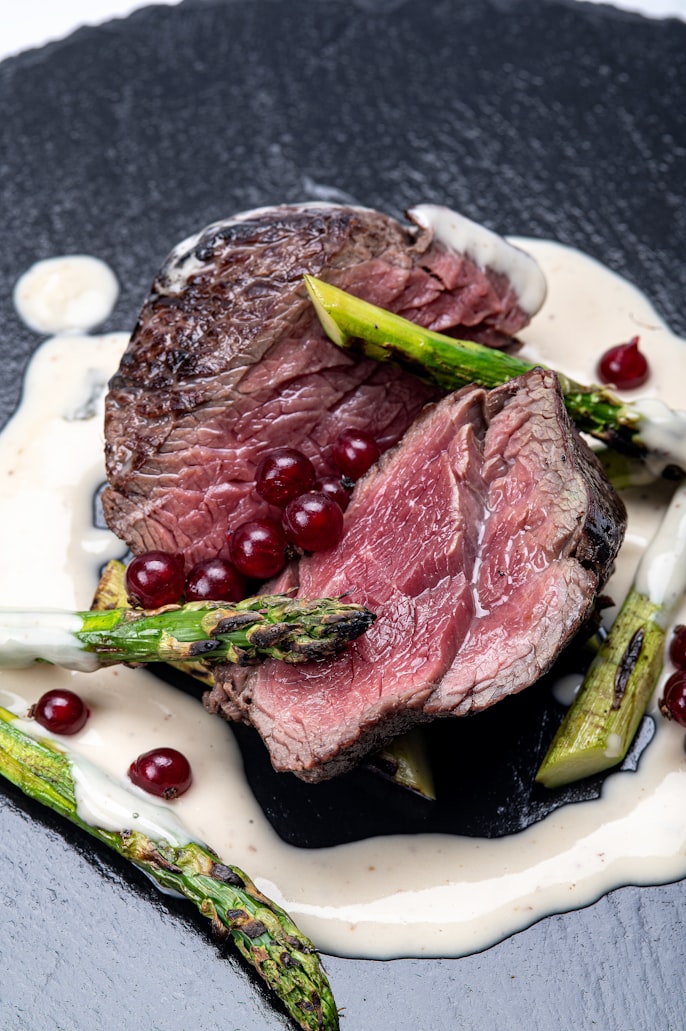Aufgeschnittenes Rehfilet, rosa gegart, mit gegrilltem Spargel und roten Beeren