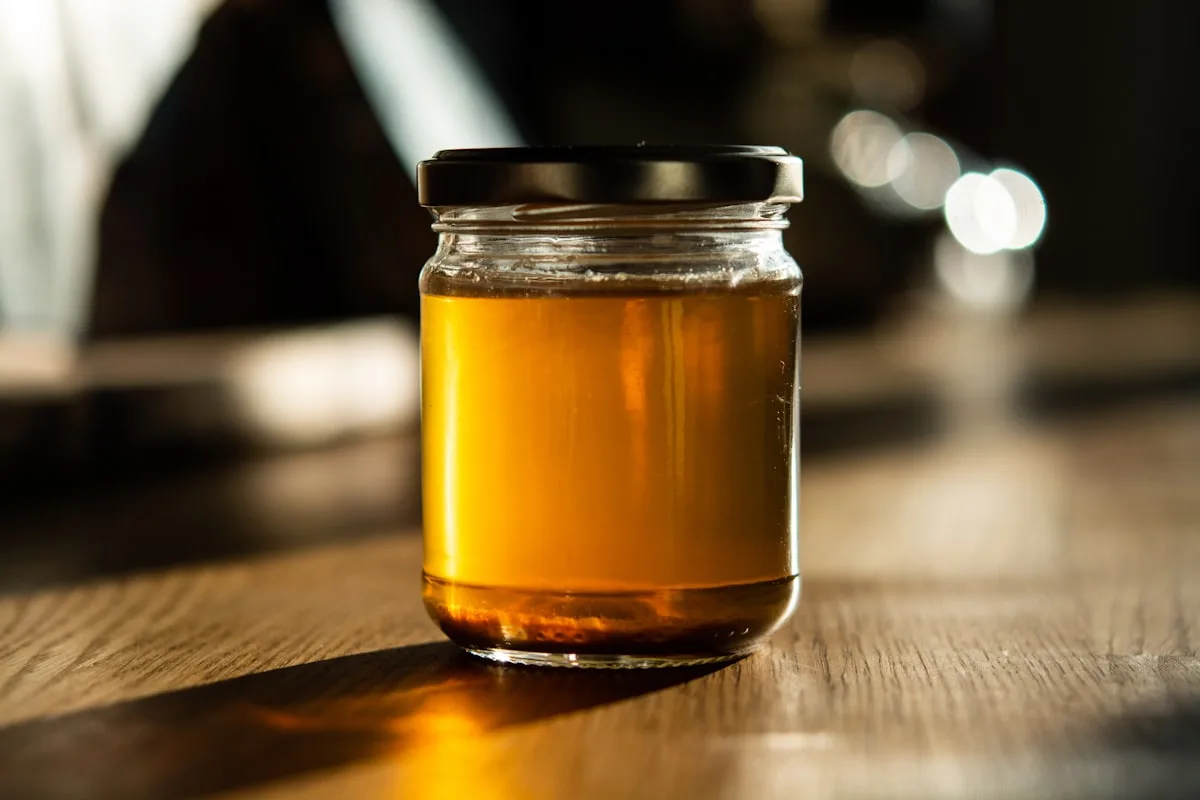Flasche mit selbstgemachtem Kräutersirup, Holunderblüten und grüne Kräuter im Hintergrund