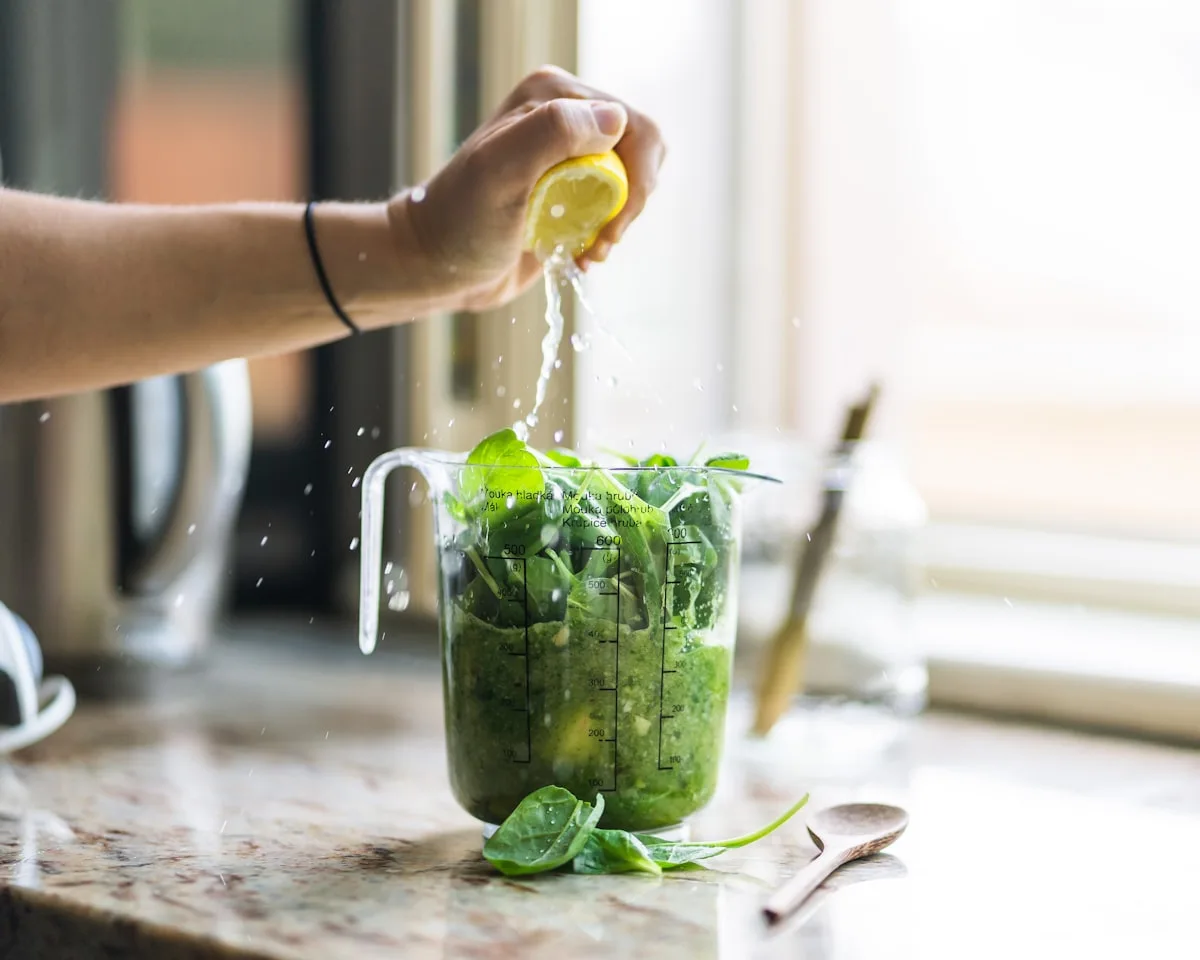 Hand presst Zitrone in Mixer mit grünen Kräutern – Pesto-Zubereitung