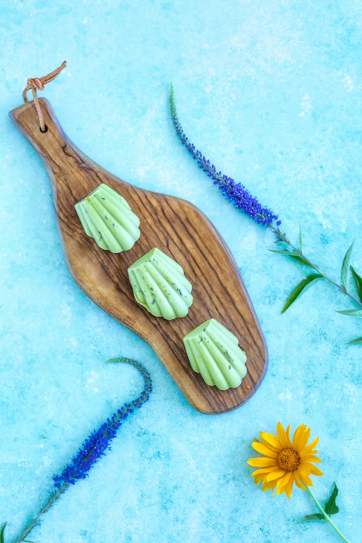 Grüne Wildkräuter-Butter in Muschelform auf einem Holzbrett, dekoriert mit frischen Blumen