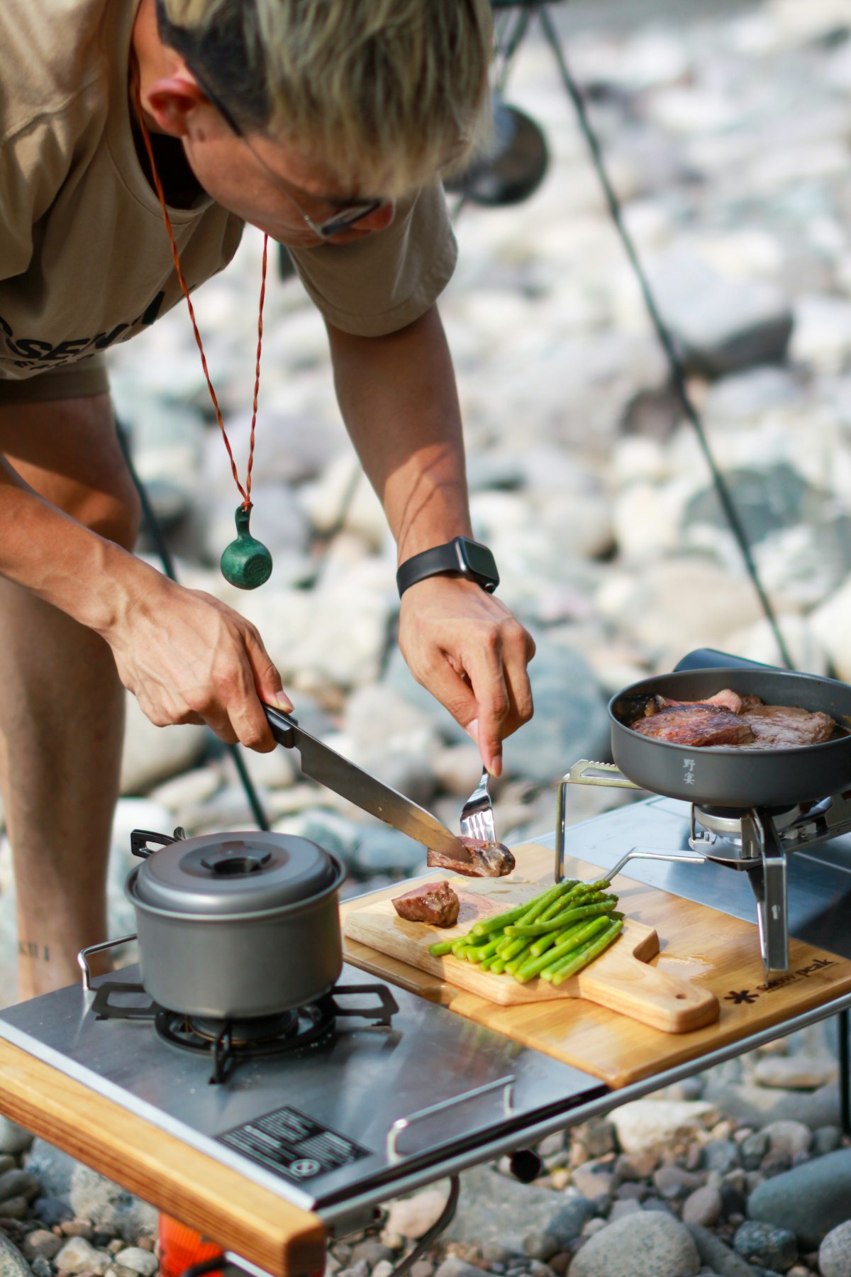 Person schneidet Fleisch auf Campingbrett draußen auf Felsen