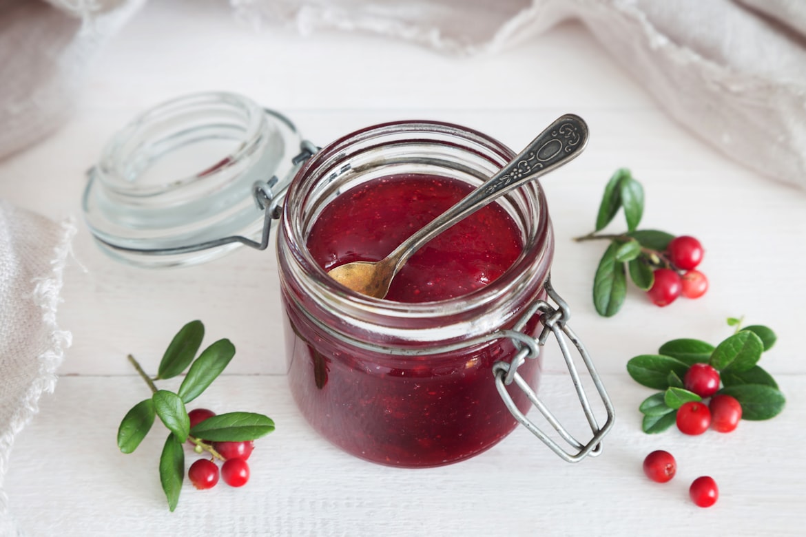 Selbst gemachtes Vogelbeeren-Gelee in einem Bügelverschlussglas mit silbernem Löffel und roten Beeren als Dekoration