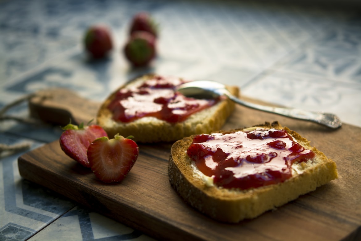 Toast mit roter Erdbeer-Konfitüre auf einem Holzbrett, frische Erdbeeren daneben